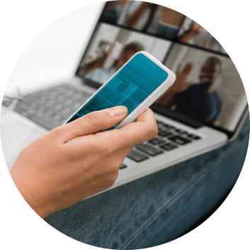 Image of a person holding a phone in hand next to a laptop.